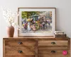 A framed painting of a flower market scene is displayed on a wooden dresser, next to a vase of white flowers. Podgląd zdjęcia produktu