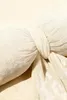A close-up view of a cream-colored velvet pillow with a knot in the center. Podgląd zdjęcia produktu