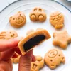 A hand is holding a cut-open pastry, with several similarly shaped pastries on a white plate in the background. The pastries are shaped like cartoon animals and vehicles, and the one being held is cut in half to reveal a dark filling. Produktbild-Vorschau
