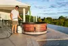 A man is filling a hot tub with a hose on a patio overlooking a landscape. Náhled obrázku produktu