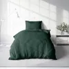 A green duvet cover and pillow are neatly arranged on a bed in a room with a white brick wall and a floor lamp. Produktbild-Vorschau