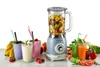 A blue vintage-style blender is shown on a white surface, surrounded by fresh fruits, vegetables, and prepared smoothies. Anteprima dell’immagine prodotto