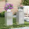 Two plant stands with potted plants on them in a garden setting. Náhled obrázku produktu