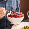 A person is holding a bowl of berries and a spoon, with a plate of pasta in the foreground. Náhled obrázku produktu
