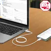 A laptop and a smartphone are connected by a white USB-C cable on a wooden table. The laptop screen shows a music syncing interface, and a red icon with a computer and phone is in the top right corner. Produktbild-Vorschau