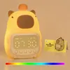 A cute capybara-shaped alarm clock with a digital display and a small card with a capybara illustration next to it. Produktbild-Vorschau