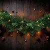 A Christmas garland with lights and pinecones is draped across a wooden background. Anteprima dell’immagine prodotto