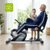An older man is exercising on a stationary bike while a young boy stands next to him, clapping. Produktbild-Vorschau