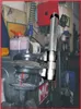 A close-up view of a tool, likely a spring compressor, in a workshop setting with various equipment in the background. Voir les images du produit