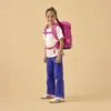A young girl wearing a pink backpack and blue jeans stands against a plain background. Produktbild-Vorschau