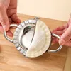Hands are using a stainless steel dumpling maker to press dough on a wooden cutting board. Produktbild-Vorschau