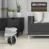 A small black and silver electric heater sits on a light-colored floor in front of a dark cabinet and a gray sofa. Produktbild-Vorschau