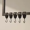 A close-up shot of black S-hooks hanging from a metal rod attached to a vertical support. Anteprima dell’immagine prodotto