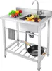 A stainless steel commercial sink with a faucet, a towel, a wok, and various fruits and vegetables on the countertop. Produktbild-Vorschau