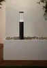A black and clear outdoor lamp stands on a textured white planter filled with stones, with a wall in the background. Produktbild-Vorschau