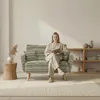 A woman is sitting on a sofa reading a book in a well-lit room. Anteprima dell’immagine prodotto