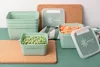 Several green food storage containers are arranged on a green surface with cork coasters and a striped cloth. Produktbild-Vorschau