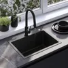 A modern kitchen sink with a black faucet and a black sink, set against a window with blooming flowers outside. Náhled obrázku produktu