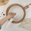 A hand is shown wiping the inside of a cream-colored pot with a white cloth, which is placed on a wooden cutting board. Produktbild-Vorschau