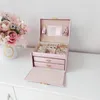 A pink jewelry box is open on a white surface, with a bouquet of pink flowers to the left. Náhled obrázku produktu