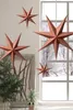 Four star-shaped ornaments hang in a room with a Christmas tree and a window showing a snowy landscape. Voir les images du produit