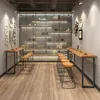 A modern cafe or bar interior with high tables and stools, featuring a wall of shelves displaying books and decorative items. Produktbild-Vorschau