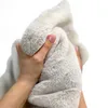 A close-up of a hand holding a soft, cream-colored faux fur mat. Produktbild-Vorschau
