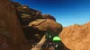 A first-person perspective of a desert environment with rocky formations and a clear blue sky. The player is holding a green glowing object. Produktbild-Vorschau