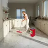 A woman is mopping a marble floor in a bright, modern kitchen. Produktbild-Vorschau