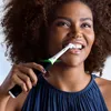 A woman is brushing her teeth with an electric toothbrush. Voir les images du produit