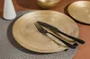 A gold-colored dessert plate with a fork and knife on it, set on a placemat. Podgląd zdjęcia produktu