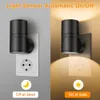 A split image showing a black LED night light plugged into a wall socket. The left side shows the light off in a gray environment, and the right side shows the light on, illuminating a tan wall. Produktbild-Vorschau