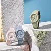 Three Casio G-Shock watches in different pastel colors are displayed on textured surfaces against a blue background. Produktbild-Vorschau