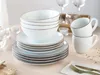 A stack of white and gray ceramic bowls and plates with brown trim, along with two white ceramic mugs, are arranged on a light-colored wooden table. Náhľad obrázku produktu