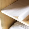 A white shelf liner unrolled on a wooden shelf. Produktbild-Vorschau
