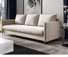 A beige sofa with three cushions sits in a well-lit room with dark blue curtains and a large framed artwork on the wall. Podgląd zdjęcia produktu