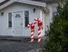 Two illuminated candy cane decorations are placed on a walkway in front of a white house. Podgląd zdjęcia produktu