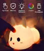 A hand is touching a cute bunny-shaped night light. The light is illuminated and shows multiple colors. There are icons and text above the product describing its features. Produktbild-Vorschau