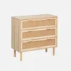 A three-drawer dresser with rattan drawer fronts and wooden legs, set against a plain light gray background.