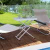 A white folding table with a pitcher and glasses of water on it, set on a wooden deck next to a chair, with a grassy yard and glass fence in the background. Produktbild-Vorschau