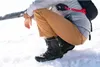 A person crouching in the snow, wearing winter boots. Produktbild-Vorschau