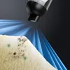 A close-up view of a vacuum cleaner nozzle emitting a blue light and spray onto a fuzzy surface with dirt and green spots. Podgląd zdjęcia produktu