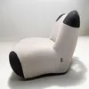 A modern, uniquely shaped armchair with dark gray accents on the 'toes' and 'ears'. Produktbild-Vorschau