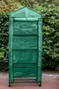 A green greenhouse with shelves is shown outdoors, with a hedge in the background. Anteprima dell’immagine prodotto