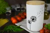 A white ceramic storage jar with a dandelion design, placed on a wooden surface with various ingredients like tomatoes, dill, and spaghetti. Produktbild-Vorschau