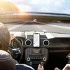 A person driving a convertible car on a sunny day, with a phone mounted on the dashboard. Náhled obrázku produktu