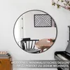 A round mirror with a black frame is mounted on a white wall above a wooden table and chairs, with a piano in the foreground. Produktbild-Vorschau