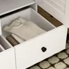 A close-up view of an open drawer in a white wardrobe, showing folded clothes. Produktbild-Vorschau