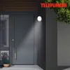 An outdoor wall light illuminates a modern gray front door. Produktbild-Vorschau