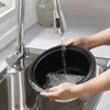 Hands holding a black inner pot under a faucet in a kitchen sink, rinsing it with water. Produktbild-Vorschau
